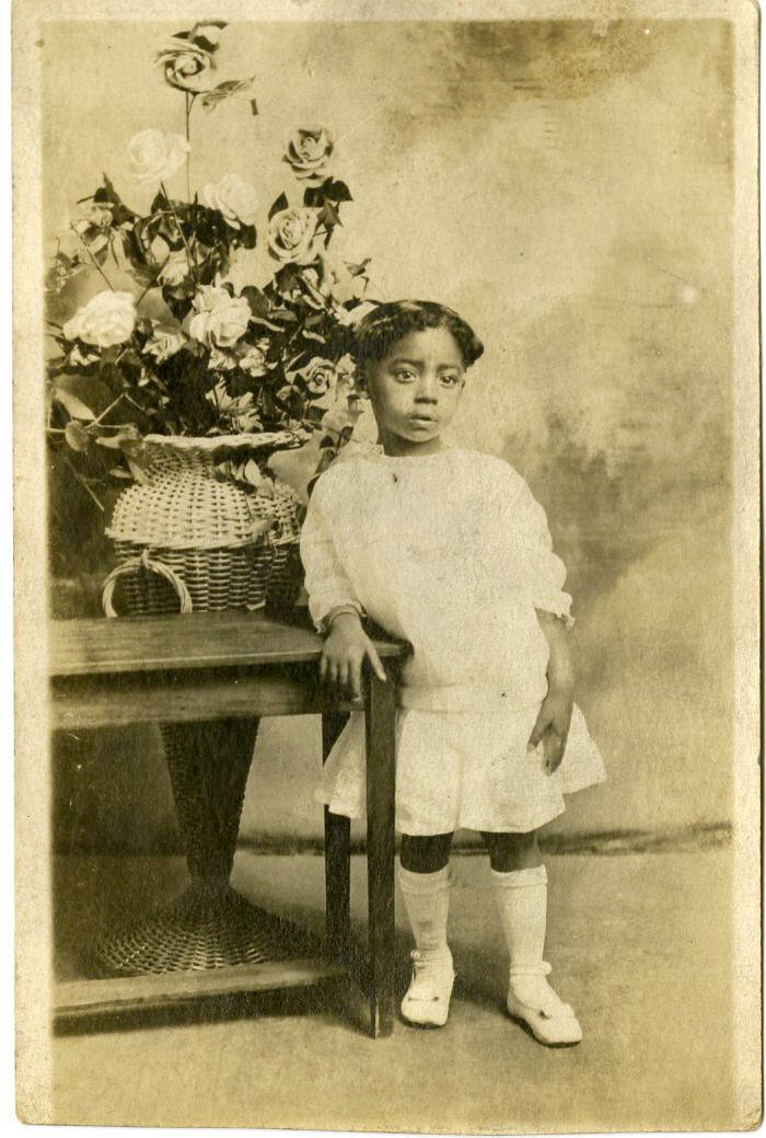 Portrait of a young girl wearing a white, knee-length skirt, a white long-sleeved sweater, and white socks that go below the knee with white shoes.
